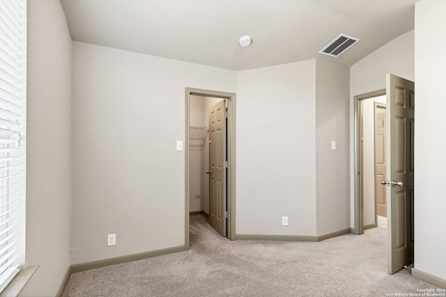 unfurnished bedroom with light colored carpet, visible vents, a spacious closet, and baseboards