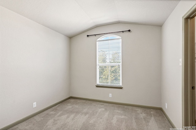 spare room with vaulted ceiling, carpet floors, and baseboards