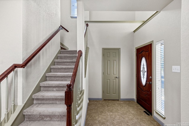 tiled entrance foyer featuring visible vents, baseboards, and stairs