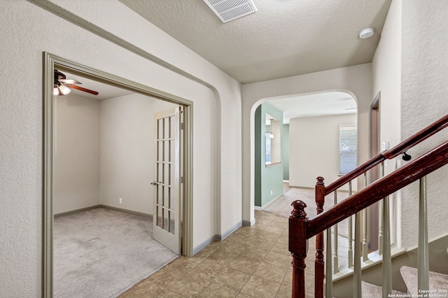 corridor featuring arched walkways, a textured ceiling, visible vents, baseboards, and carpet