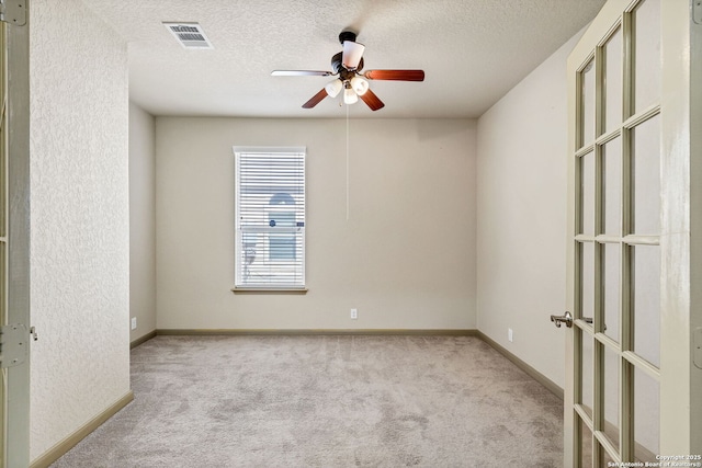 carpeted empty room with a textured ceiling, ceiling fan, visible vents, and baseboards