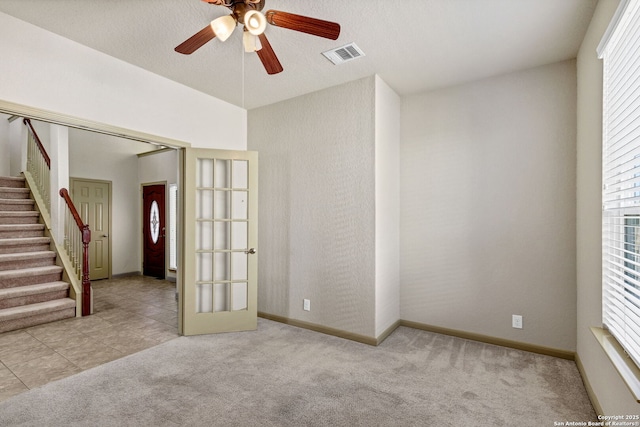 carpeted spare room with ceiling fan, tile patterned flooring, visible vents, baseboards, and stairway