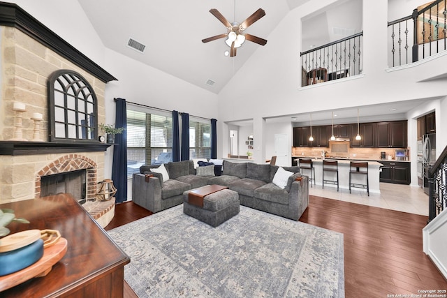 living area featuring a fireplace with raised hearth, ceiling fan, light wood-type flooring, and visible vents