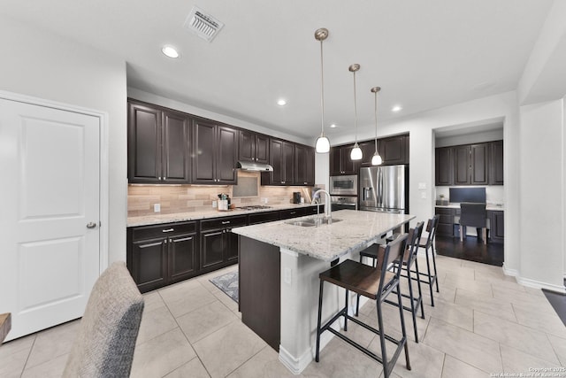 kitchen featuring stainless steel appliances, visible vents, a sink, under cabinet range hood, and a kitchen bar