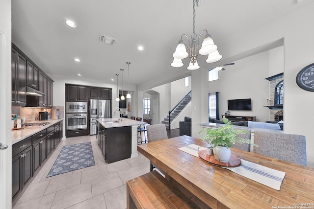 kitchen featuring arched walkways, an inviting chandelier, a kitchen island with sink, stainless steel appliances, and a sink