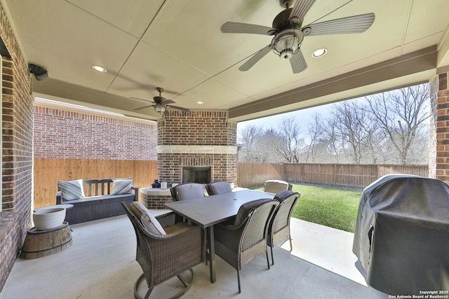 view of patio / terrace with outdoor dining area, a fenced backyard, area for grilling, a ceiling fan, and an outdoor brick fireplace