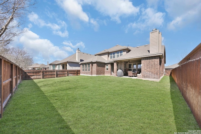 rear view of house featuring a patio, a fenced backyard, brick siding, a lawn, and a chimney