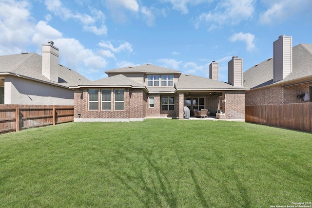 back of property featuring a patio, a fenced backyard, a chimney, a yard, and brick siding