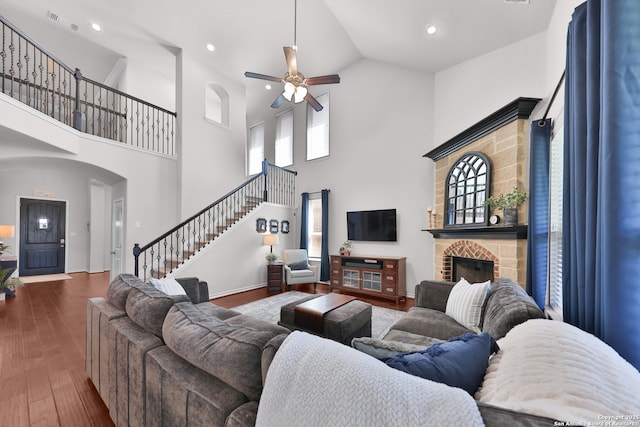 living room with a stone fireplace, visible vents, a ceiling fan, stairs, and dark wood finished floors