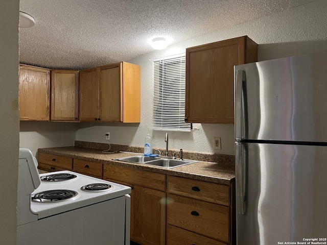 kitchen with a textured ceiling, a sink, freestanding refrigerator, dark countertops, and white electric range oven