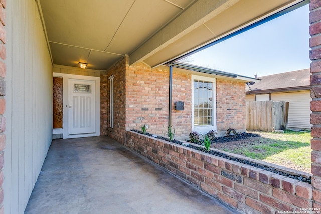 doorway to property featuring brick siding and fence