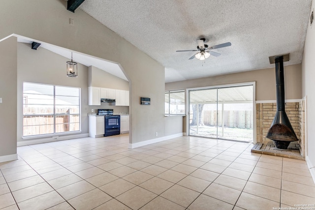 unfurnished living room featuring light tile patterned floors, ceiling fan, a wood stove, and vaulted ceiling with beams