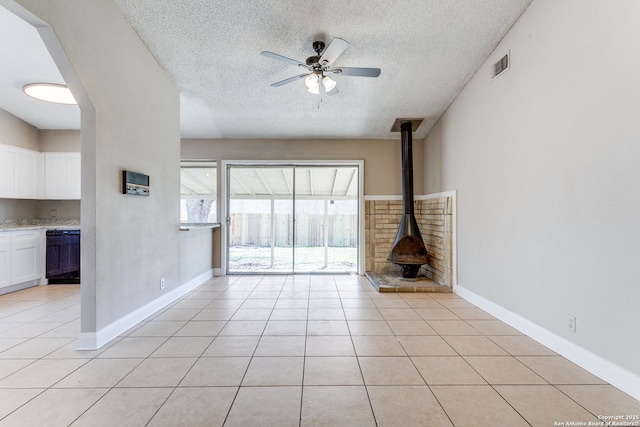 unfurnished living room featuring light tile patterned floors, a wood stove, ceiling fan, and visible vents