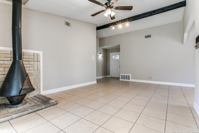 unfurnished living room featuring visible vents, light tile patterned floors, beamed ceiling, and a wood stove