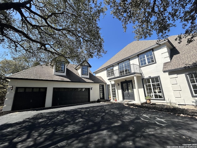 view of front of home featuring a garage, aphalt driveway, a balcony, and stucco siding