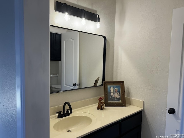 bathroom featuring toilet, a textured wall, and vanity