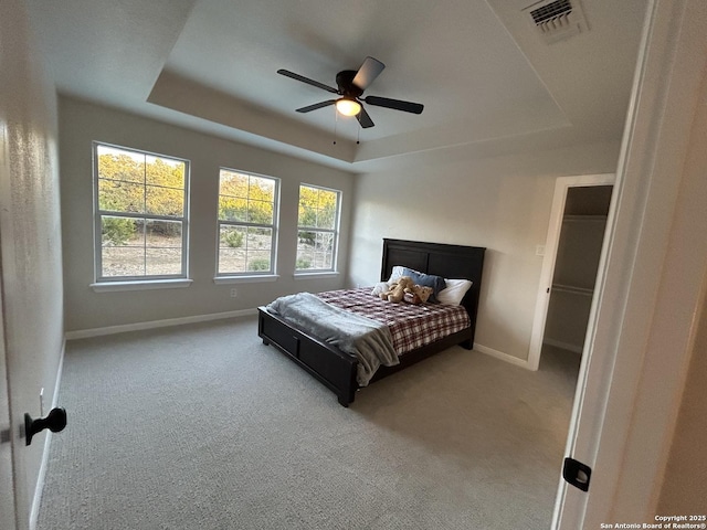 carpeted bedroom with a raised ceiling, multiple windows, visible vents, and baseboards