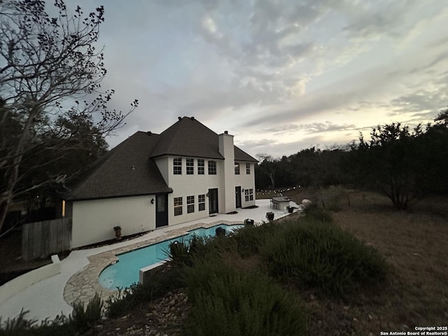 rear view of property featuring a patio area, an outdoor pool, and a chimney