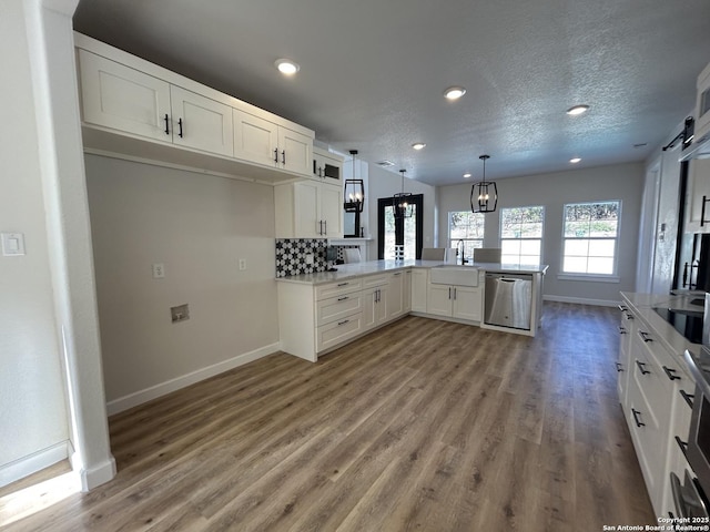 kitchen featuring light wood finished floors, a peninsula, stainless steel dishwasher, white cabinetry, and a sink