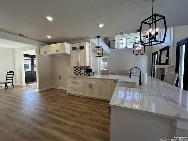 kitchen featuring visible vents, an inviting chandelier, white cabinetry, a sink, and light stone countertops