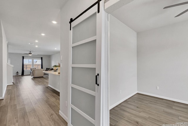 hall featuring a barn door, recessed lighting, wood finished floors, and baseboards