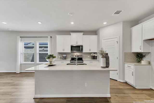 kitchen with stainless steel appliances, tasteful backsplash, light wood-style floors, white cabinetry, and a sink