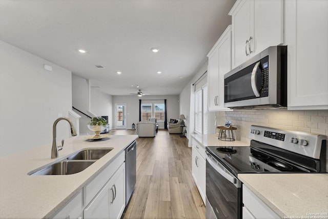 kitchen with light wood finished floors, decorative backsplash, appliances with stainless steel finishes, white cabinets, and a sink