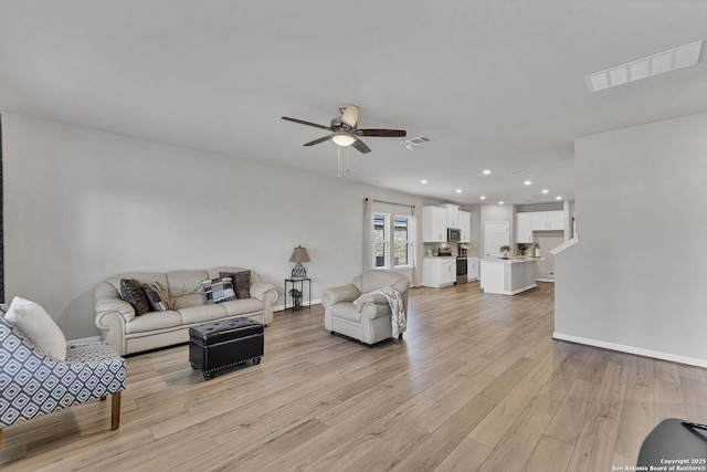 living room with light wood-style floors, visible vents, ceiling fan, and baseboards