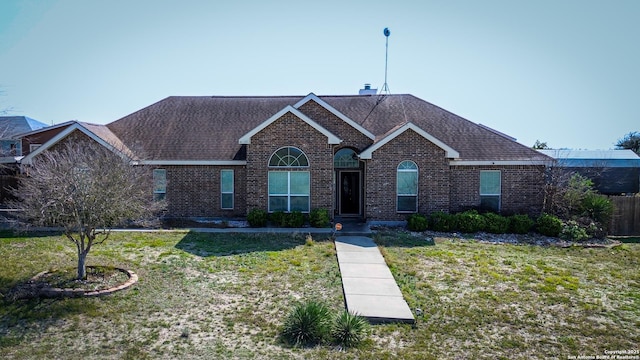 single story home featuring brick siding, a front yard, and a shingled roof