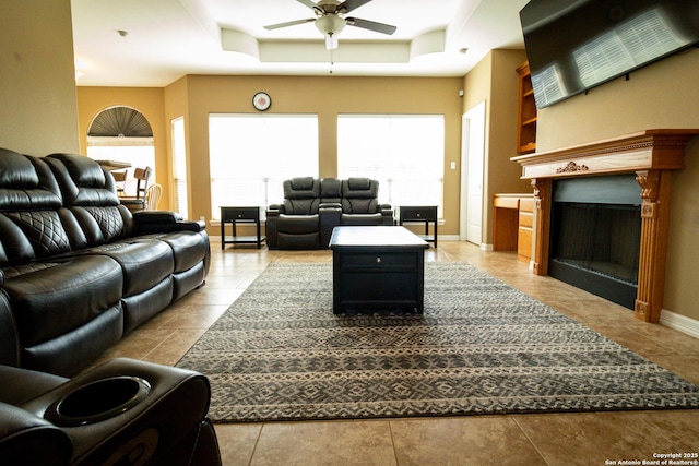 living area with a tray ceiling, a fireplace, a ceiling fan, and baseboards