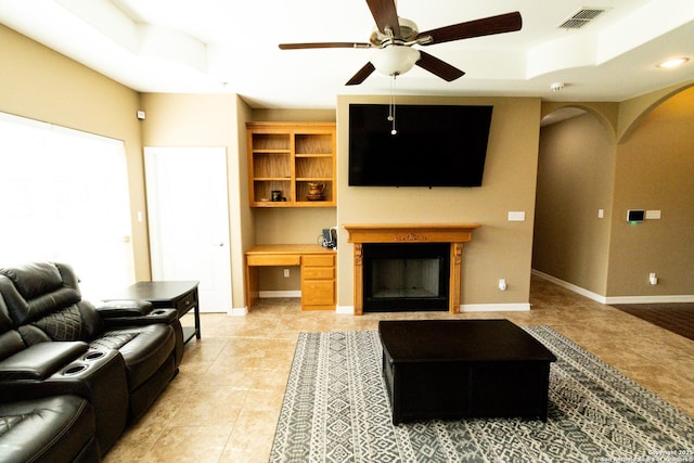 living room featuring a raised ceiling, built in study area, visible vents, and baseboards