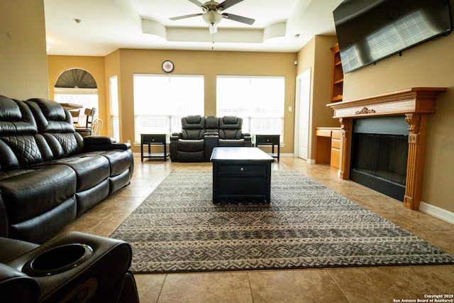 living room featuring ceiling fan, a fireplace, baseboards, and a raised ceiling