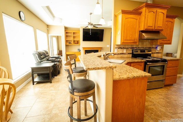 kitchen with under cabinet range hood, open floor plan, a sink, and stainless steel range with electric cooktop