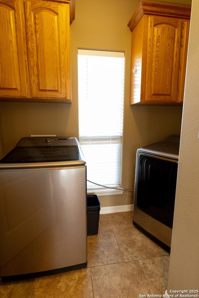 clothes washing area with light tile patterned floors, cabinet space, and baseboards