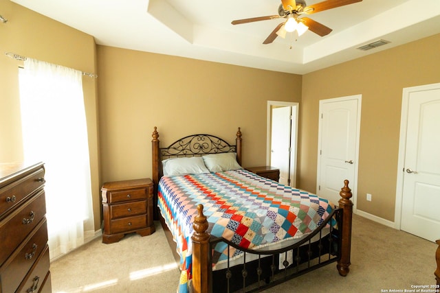 bedroom featuring light carpet, visible vents, baseboards, a ceiling fan, and a tray ceiling