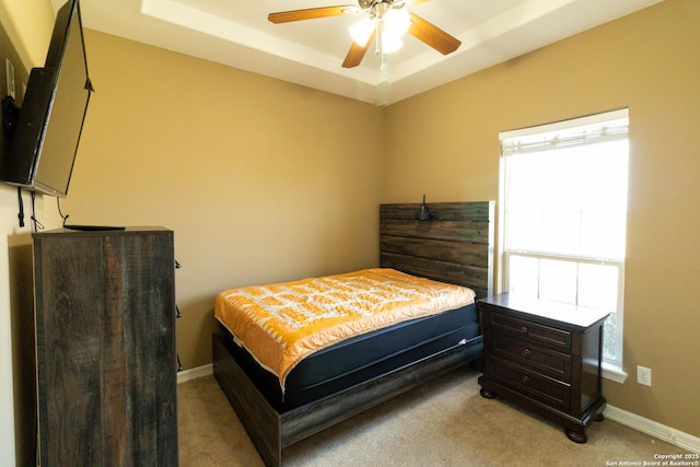 bedroom featuring light carpet, ceiling fan, a tray ceiling, and baseboards