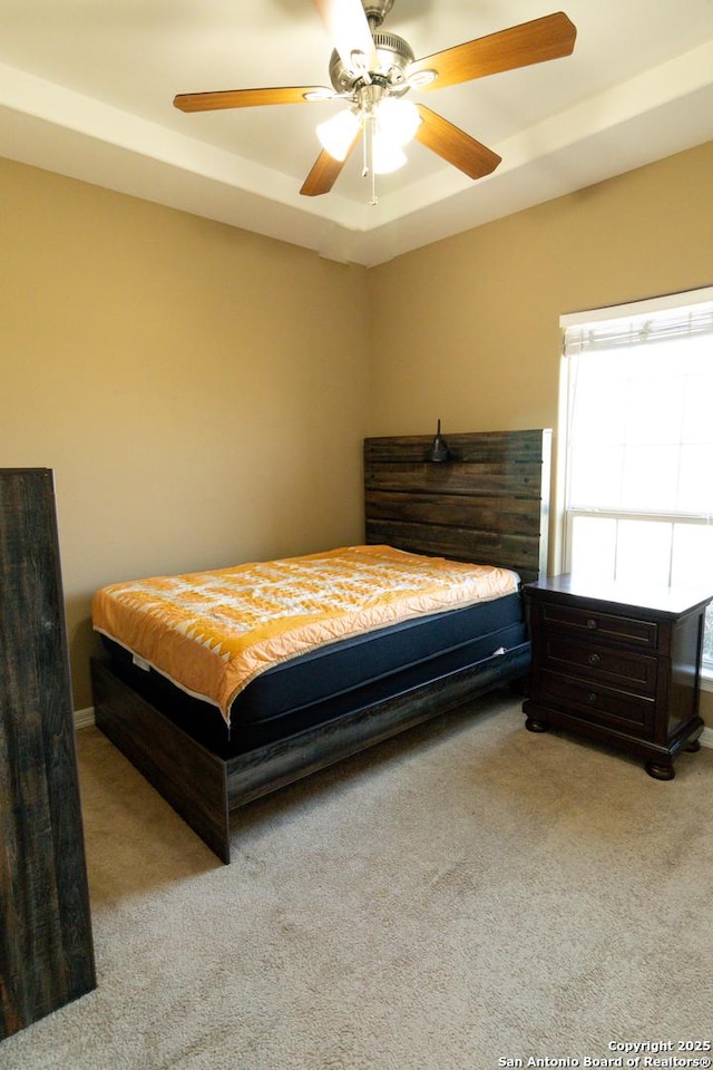 bedroom with a tray ceiling, a ceiling fan, and light colored carpet