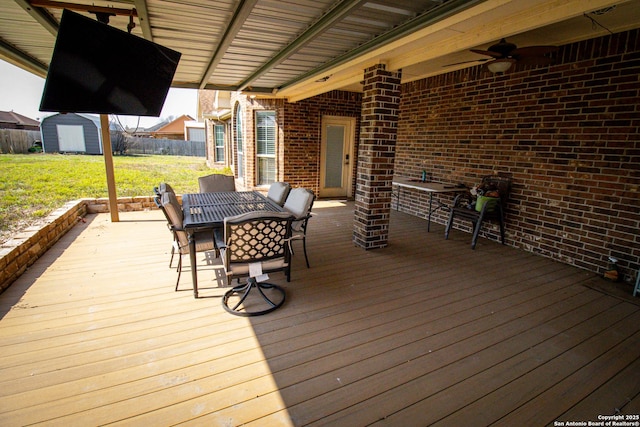 wooden deck featuring an outbuilding, outdoor dining area, a yard, fence, and a shed