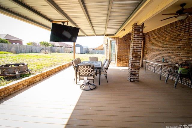 deck featuring an outbuilding, outdoor dining area, a storage unit, ceiling fan, and a fenced backyard