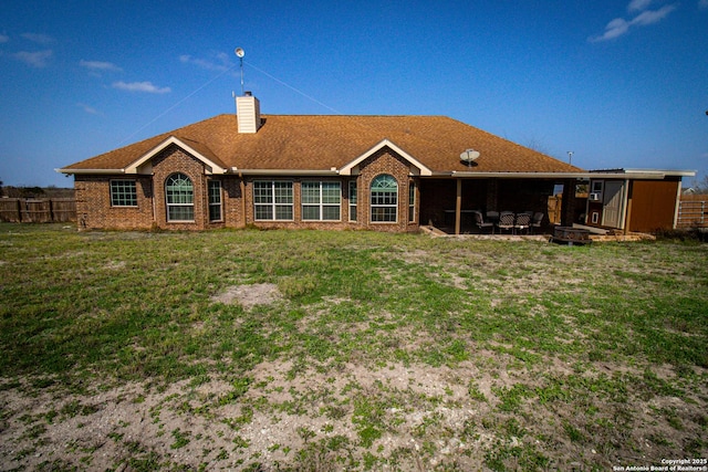 back of house with a chimney, fence, a lawn, and brick siding