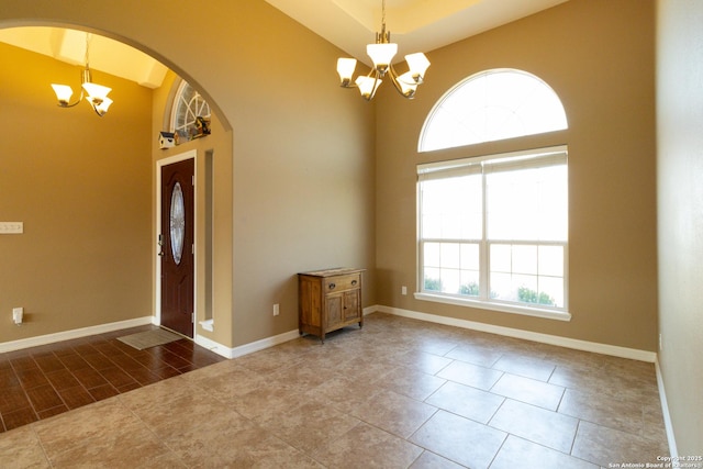 entrance foyer featuring arched walkways, baseboards, a towering ceiling, and a notable chandelier