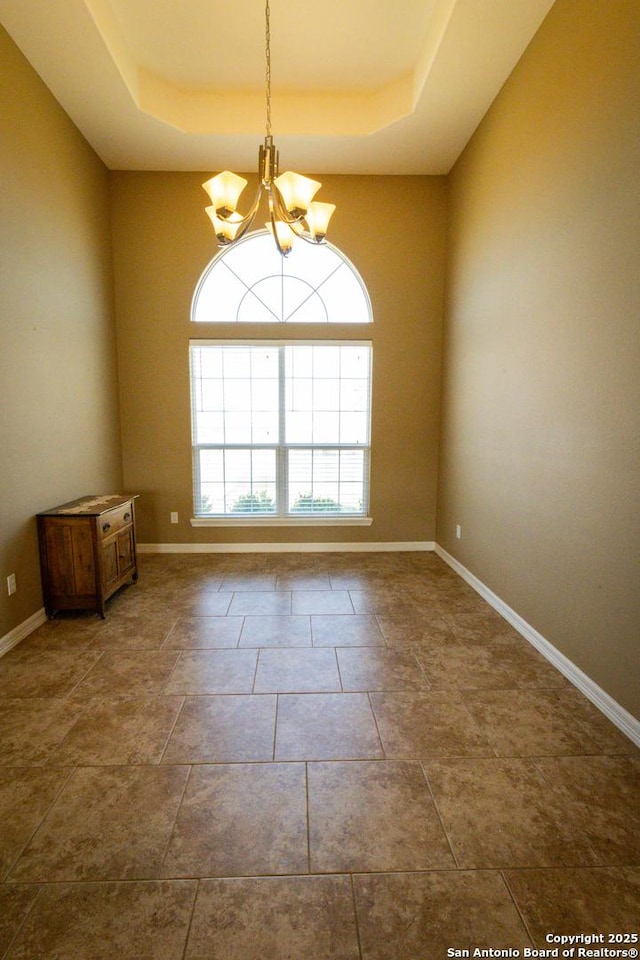 unfurnished room with a tray ceiling, baseboards, and an inviting chandelier