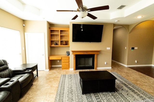 living area featuring ceiling fan, a fireplace, visible vents, baseboards, and built in study area