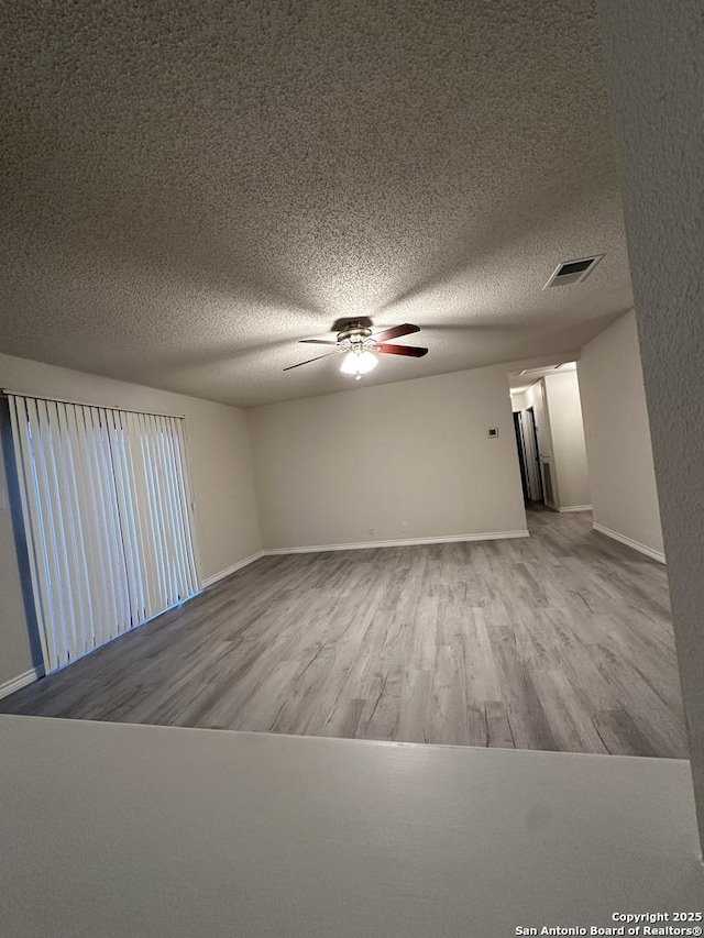 spare room with a textured ceiling, wood finished floors, a ceiling fan, and baseboards