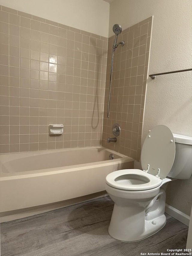 full bath featuring washtub / shower combination, a textured wall, toilet, and wood finished floors