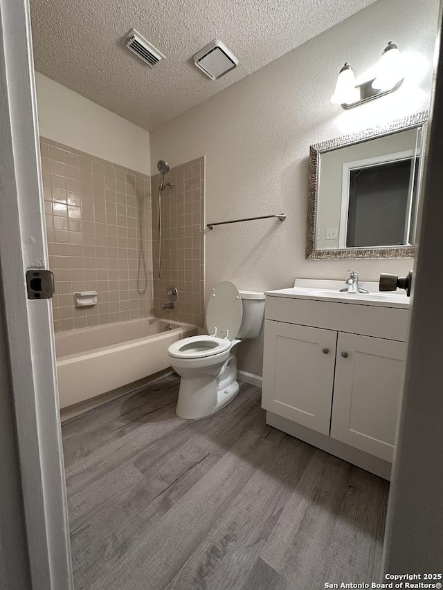 bathroom with a textured ceiling, toilet, wood finished floors, visible vents, and shower / bathing tub combination