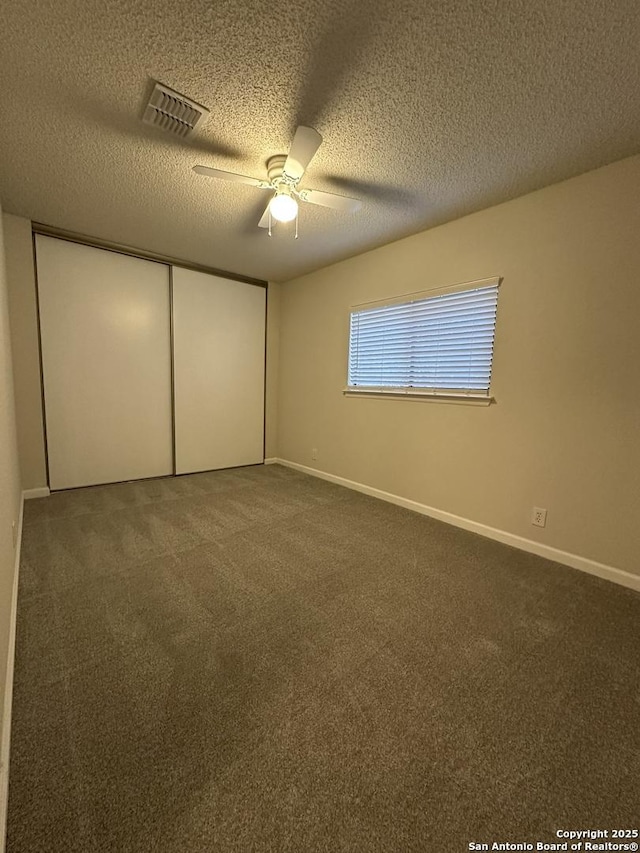 unfurnished bedroom with baseboards, visible vents, dark carpet, and a closet