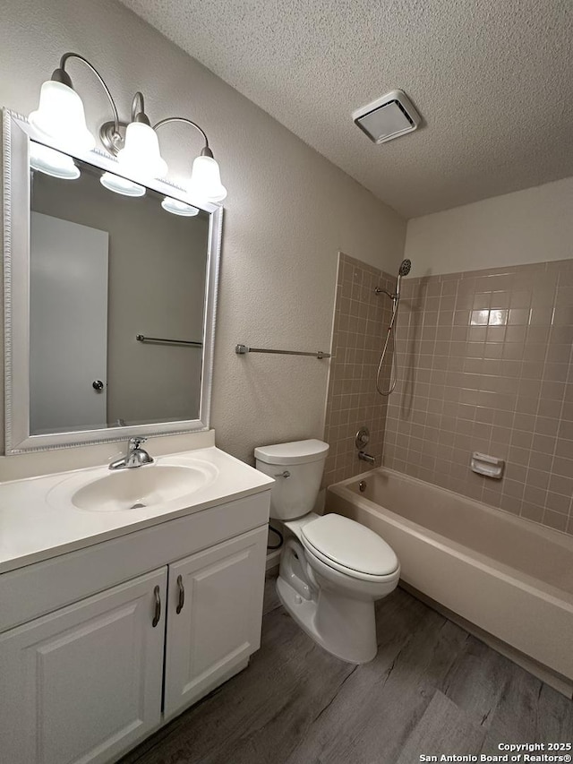 full bath featuring a textured ceiling, a textured wall, toilet, wood finished floors, and vanity