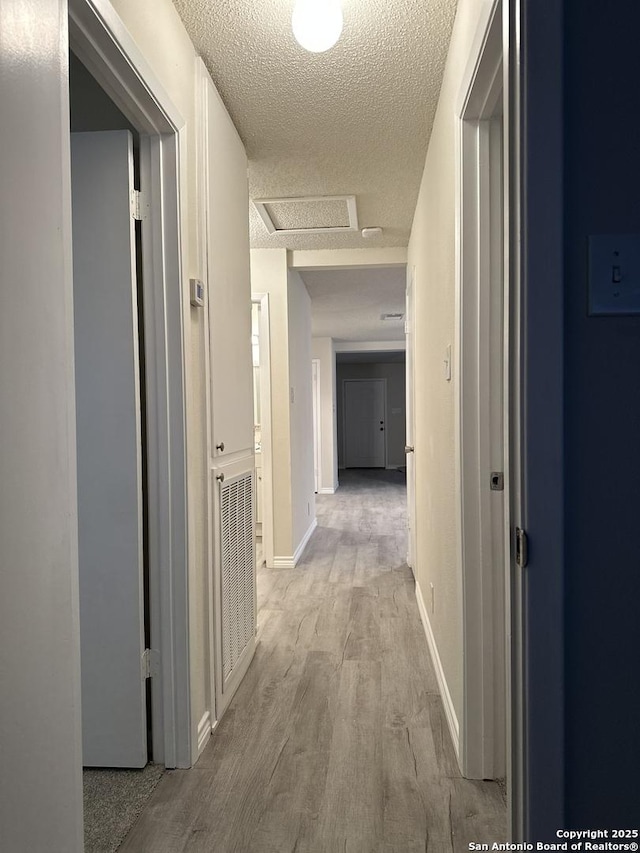 hall featuring light wood finished floors, visible vents, attic access, a textured ceiling, and baseboards