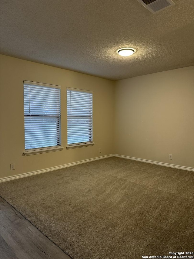 carpeted spare room with a textured ceiling, wood finished floors, visible vents, and baseboards